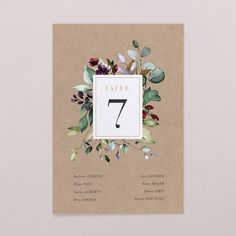 a table number card with flowers and leaves on the front, in brown paper against a white background