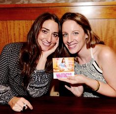 two women sitting at a table posing for the camera with a card in front of them