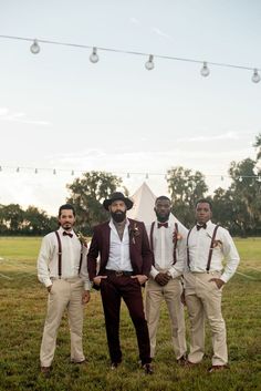 three men in ties and vests standing next to each other on grass with string lights above them