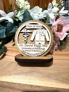 a wooden plaque with an image of a doctor's coat on it and flowers in the background