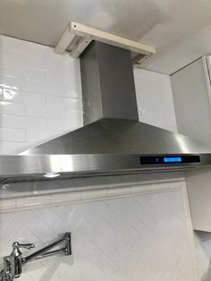 a stainless steel range hood in a kitchen with white tiles on the walls and floor