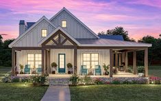 a house that is sitting in the grass with flowers on the front lawn and porch