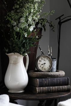 a white vase sitting on top of a stack of books next to a clock