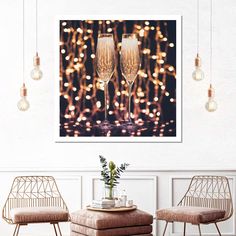 two champagne glasses sitting on top of a table next to a wall with lights in the background