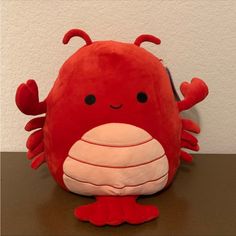 a red stuffed crab sitting on top of a table next to a white wall with black eyes