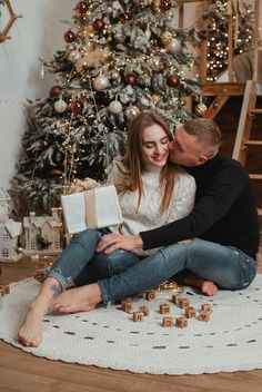 a man and woman sitting next to a christmas tree with presents in front of them