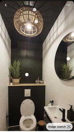 a white toilet sitting next to a bathroom sink under a round light above a mirror