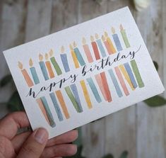 a hand holding up a birthday card with candles on it and the words happy birthday written in black ink