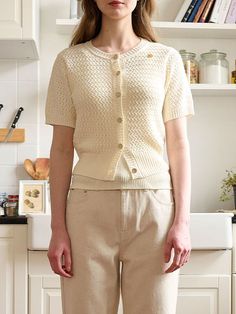 a woman standing in a kitchen wearing beige pants and a cardigan sweater with buttons