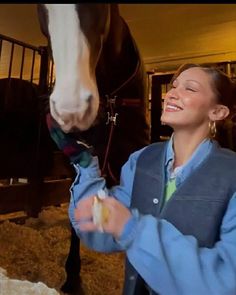 a woman standing next to a horse holding something in it's mouth and smiling