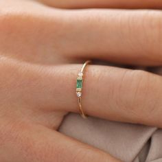 a woman's hand wearing a gold ring with an emerald and white diamond band