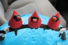 three red birds are sitting on a branch in front of a blue frosted cake