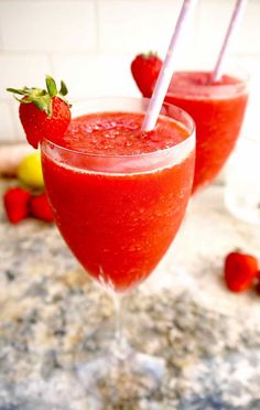 two glasses filled with red liquid and strawberries next to each other on a counter