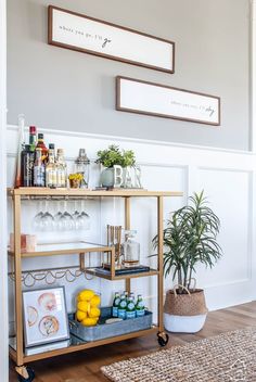 a bar cart with drinks on it next to a potted plant and framed pictures