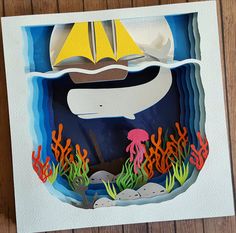 a paper cut out of an ocean scene with a boat and jellyfish on the water