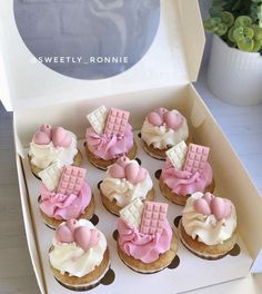 twelve cupcakes in a box with pink icing and white frosting on top