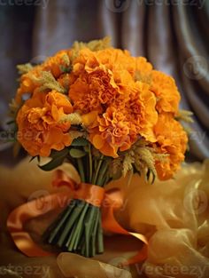 a bouquet of orange flowers sitting on top of a yellow cloth covered tablecloth next to an orange ribbon