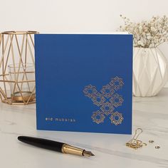 a blue greeting card with an intricate cross on it next to a pen and vase