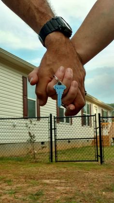 two people holding hands over a fence with a house in the back ground behind them