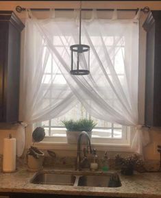 a kitchen sink under a window covered in white curtains