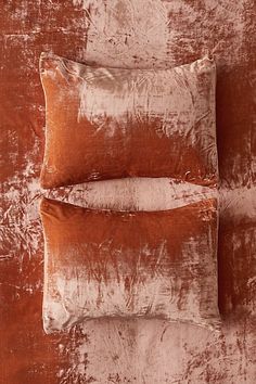 two brown velvet pillows sitting on top of a bed next to an orange and white wall