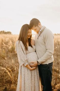 a pregnant couple standing in a field with the sun shining down on them and holding each other