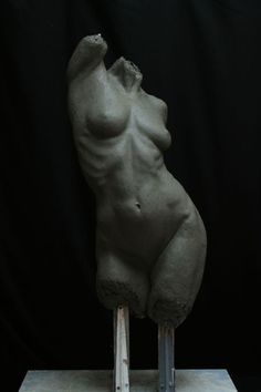 a sculpture of a naked woman standing on a wooden stand with one leg raised up