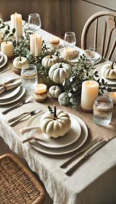 a table set with white pumpkins, candles and greenery on top of it