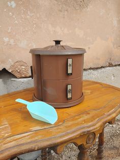 a wooden table topped with a brown container and a blue spoon sitting on top of it