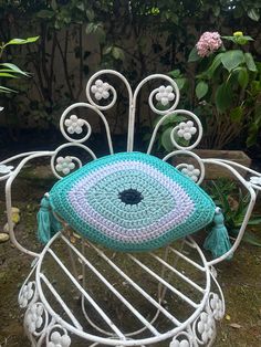 a crocheted peacock pillow sitting on top of a white metal chair in the grass