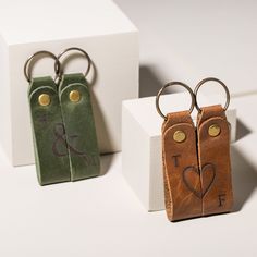 two leather keychains with initials on them sitting next to each other in front of a white box