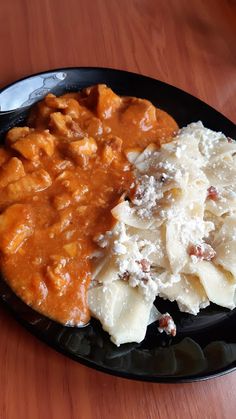 a black plate topped with macaroni and cheese covered in gravy on top of a wooden table