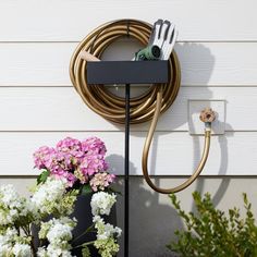 a garden hose is attached to the side of a house with flowers in front of it