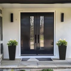 two planters on the front steps of a house with black doors and sidelights