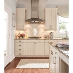 a large kitchen with white cabinets and wood flooring, including an oven hood over the stove