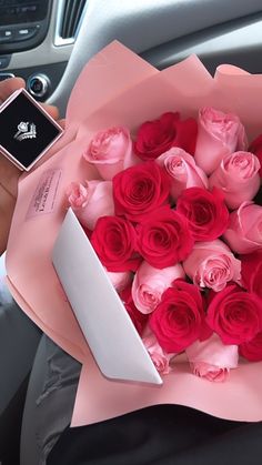 a person holding a bouquet of pink roses in their hand and a cell phone on the car seat