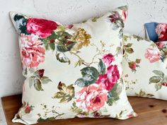 two floral pillows sitting on top of a wooden shelf next to a phone charger