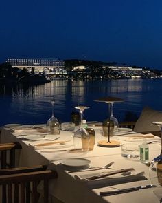 the table is set with wine glasses, plates and utensils in front of an ocean view at night