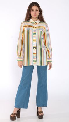 "Vintage 70s shirt in white with rainbow stripes. Buttons down the chest with long sleeves and a collar. Every garment we sell is authentic vintage and one-of-a-kind! You will receive the exact item photographed. Condition: Very good vintage. Best fits women's: Small to medium Material: Feels like Polyester MEASUREMENTS Taken from seam to seam while the garment is lying flat. Double the armpit, waist, and hips For reference, model is 5'5\" and measures 32-24-34. Length from Top: 27\" Armpit to A Multicolor Long Sleeve Top With Vertical Stripes, Retro Spring Top With Rainbow Print, Retro Rainbow Print Top For Spring, Retro Rainbow Tops For Spring, Vintage Multicolor Tops With Button Closure, Retro Multicolor Button-up Shirt, Retro White Long Sleeve Shirt, Retro Striped Collared Blouse, Vintage Striped Tops With Button Closure