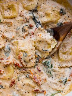 a wooden spoon is in a bowl filled with pasta and vegetables, topped with cheese