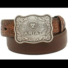 Style number: A1301002 Brown full-grain leather belt. Floral tooled design on billets. 1/4 inch belt width. Antique silver large square belt buckle with scroll filigree and Ariat shield logo and roped scalloped edges. Square Belt Buckle, Tooled Belt, Boys Belt, Little Cowboy, Shield Logo, Tool Belt, Branded Belts, Leather Floral, Western Belts