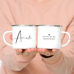 two white coffee mugs with names on them held in front of a woman's face