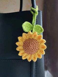 a crocheted sunflower is attached to a black leather handbag with green leaves