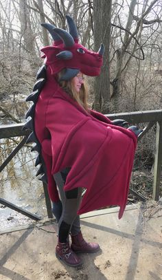 a woman in a red dragon costume standing on a wooden deck next to a tree