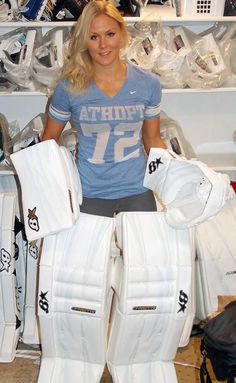 a woman standing next to some white hockey goalie gear in a room filled with sports equipment