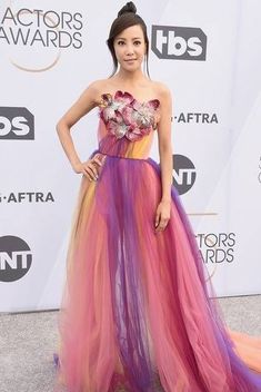 a woman in a colorful dress standing on the carpet at an awards event with her hands on her hips