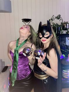 two women dressed up as batman and catwoman posing for the camera with balls in their hands