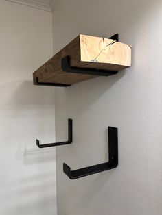 two black brackets are attached to the wall and one is holding a wooden object on it's side