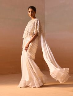 Make a statement in this ivory satin pre-draped sari, paired with a bustier and a beautifully embellished poncho in net. The poncho features intricate detailing with pearls and silver nalki zircons, adding a touch of elegance and sophistication to your ensemble. Luxury White Pre-draped Saree With Dupatta, Luxury Off White Pre-draped Saree With Cutdana, Luxury Off-white Pre-draped Saree With Cutdana, Luxury White Pre-draped Saree With Pearl Embroidery, Off White Pre-draped Cutdana Saree, Cotton Sarees Handloom, White Poncho, Dhoti Saree, White Cape