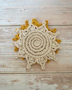 a crocheted doily is laying on a wooden surface with yellow and white accents